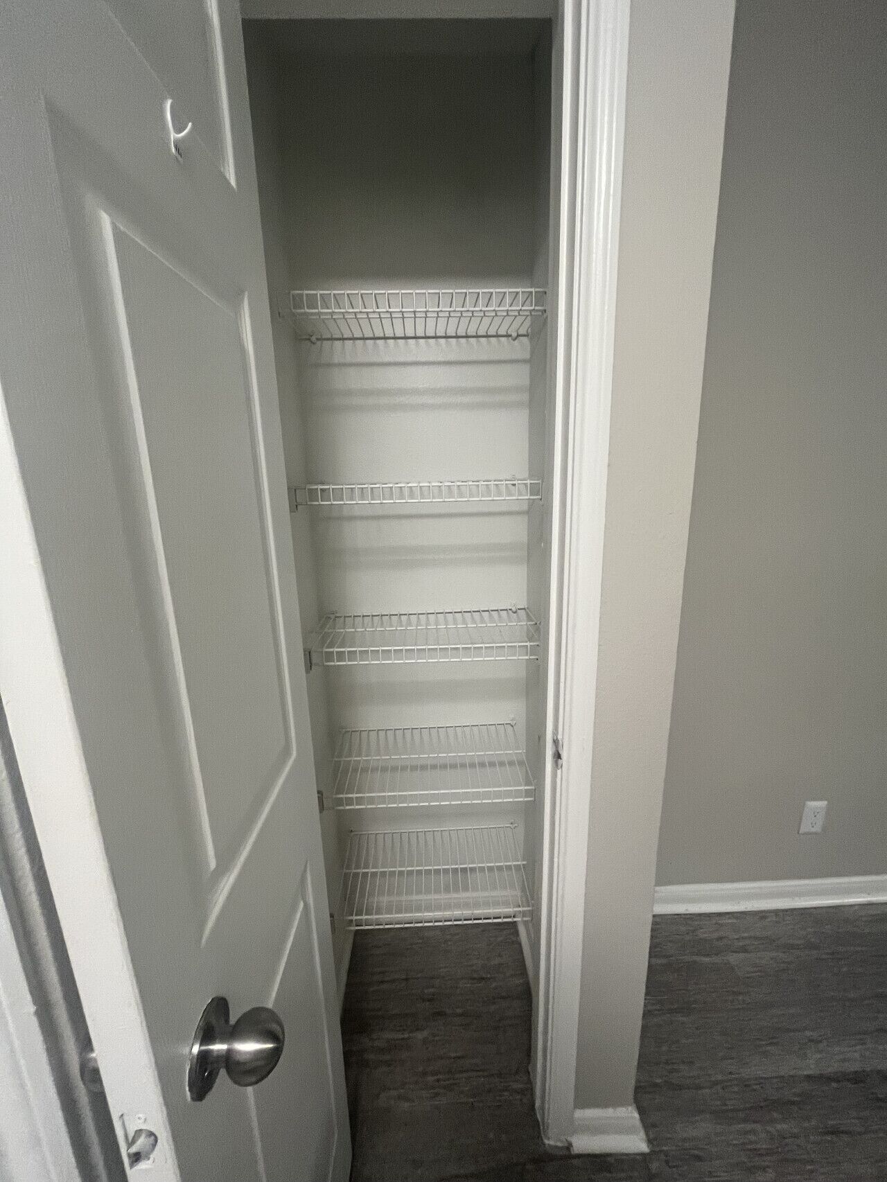 Um corredor estreito, com uma porta branca à esquerda e um armário branco com três prateleiras à direita.