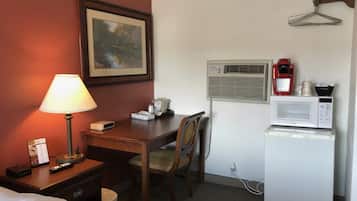 A hotel room with a bed, a desk with a lamp, a chair, a microwave, and a coffee maker.