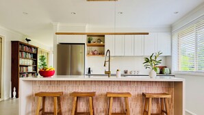 Una cocina moderna con una isla central, taburetes de bar, una estantería y un refrigerador.
