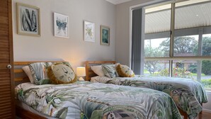 Un dormitorio con dos camas, cada una con una colcha estampada y un almohadón con forma de león. Hay cuadros enmarcados en la pared, una ventana con vistas al exterior y una puerta de madera.