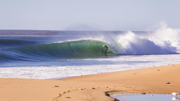 Una playa con un surfista montando una ola grande.