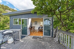 A modern cabin with a deck, a dining area, and a large window overlooking a forested area.