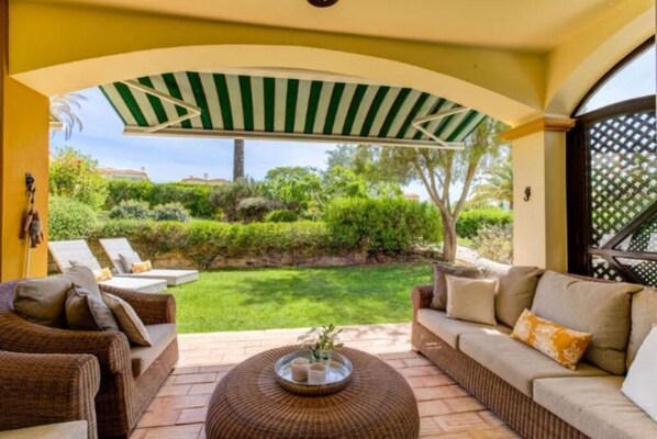 A patio area with wicker furniture, a round coffee table, and a view of a well-maintained garden.