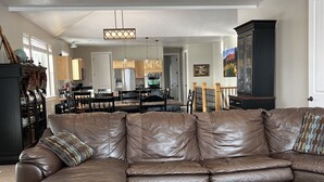 Ein geräumiges Wohnzimmer mit einem großen braunen Ledersofa, einem Holztisch und einer Küche im Hintergrund.