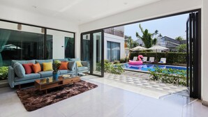 A modern living room with a sofa, coffee table, and a view of a swimming pool with lounge chairs. - Chieu Ha Village (Da Nang)