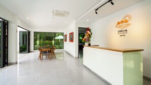 A modern reception area with a wooden reception desk, a glass partition, and a logo on the wall. - Chieu Ha Village (Da Nang)