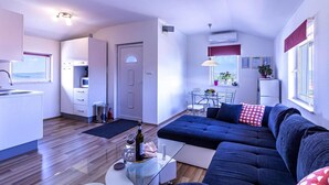 A modern living room with a dark blue sofa, a glass coffee table, and a dining area with a white table and chairs.