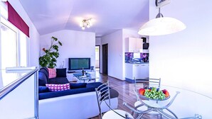 A modern living room with a sofa, TV, and dining area with a glass table and chairs.