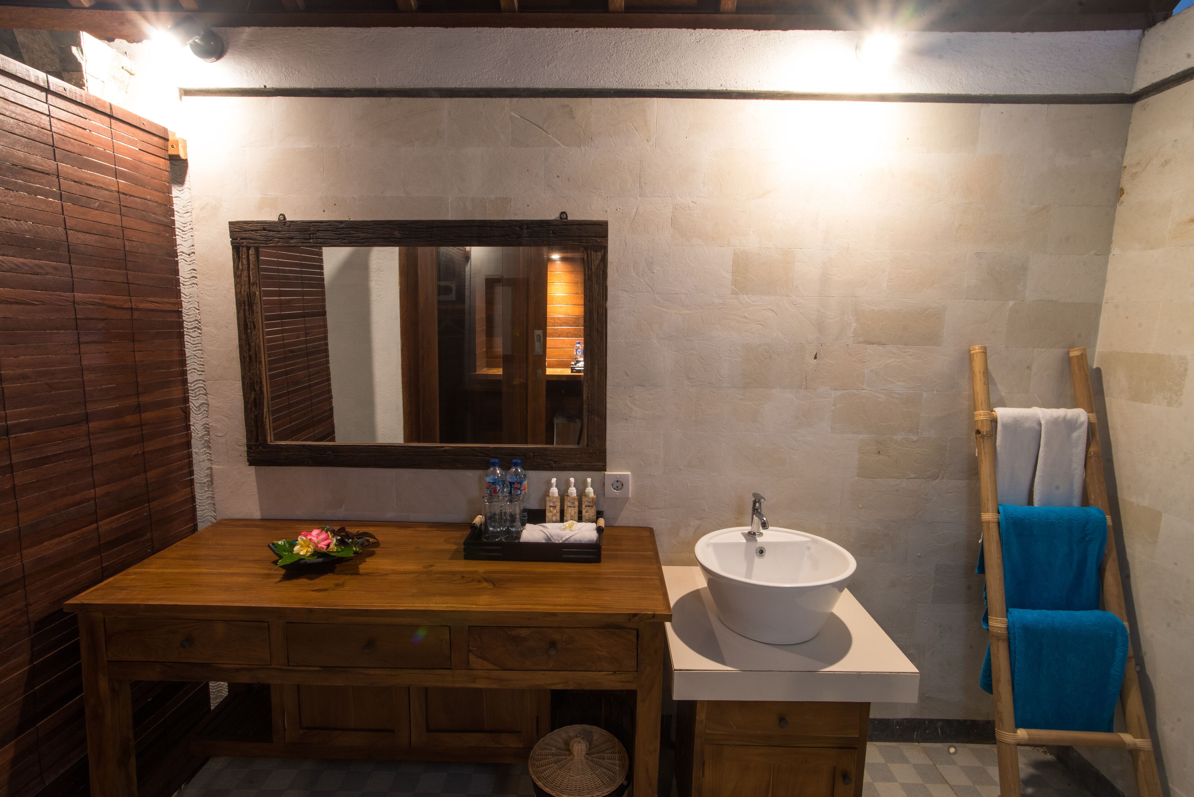 Un baño con tocador de madera, un lavabo blanco y un espejo. Hay una escalera de madera con toallas y un cesto de artículos de aseo en el tocador.
