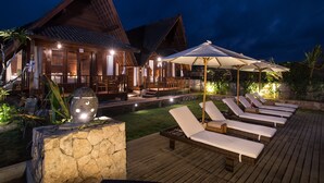 A wooden villa with a deck, lounge chairs, and umbrellas.