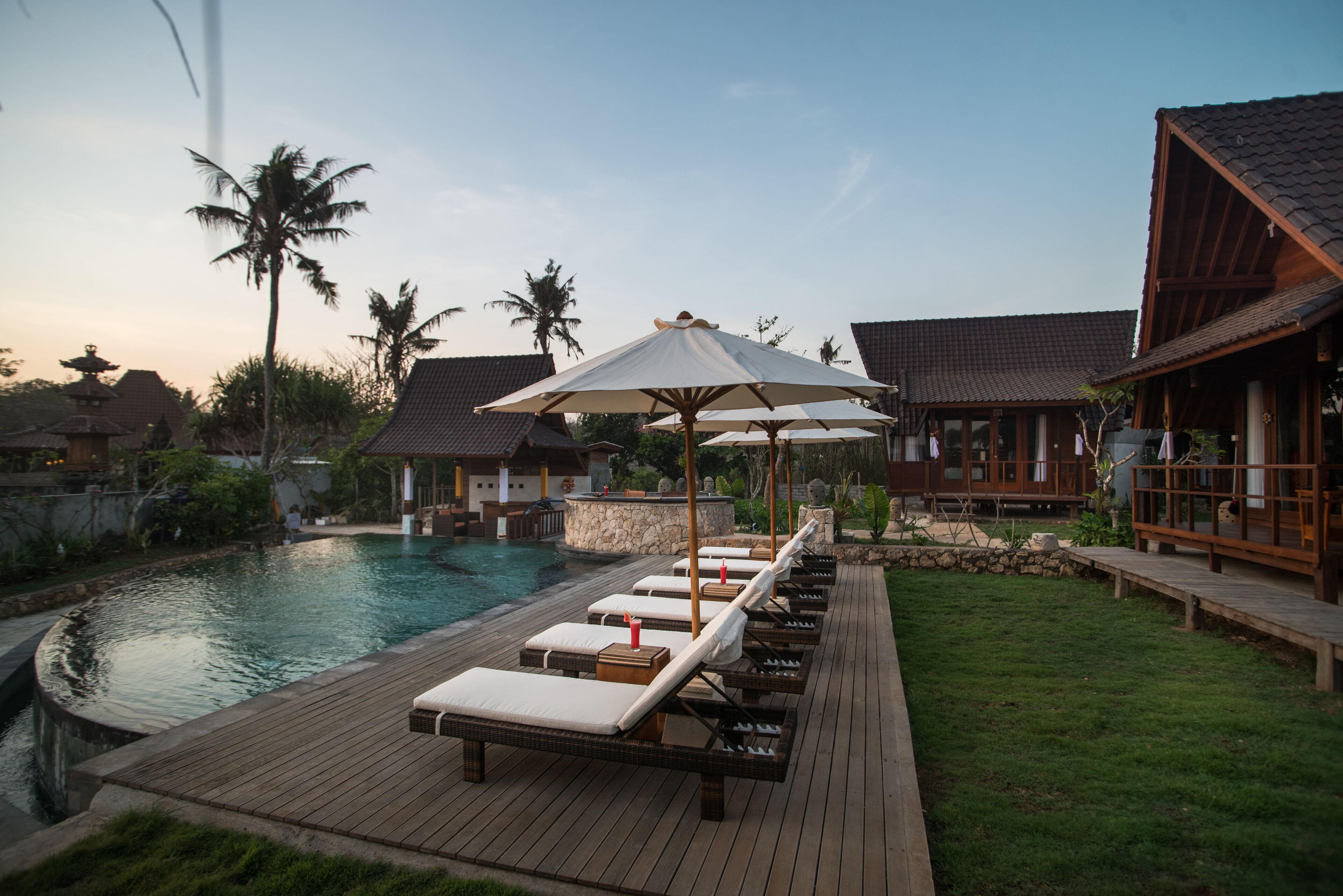 Un espace aménagé au bord de la piscine, avec des chaises longues et des parasols, une terrasse en bois et un mur en pierre.