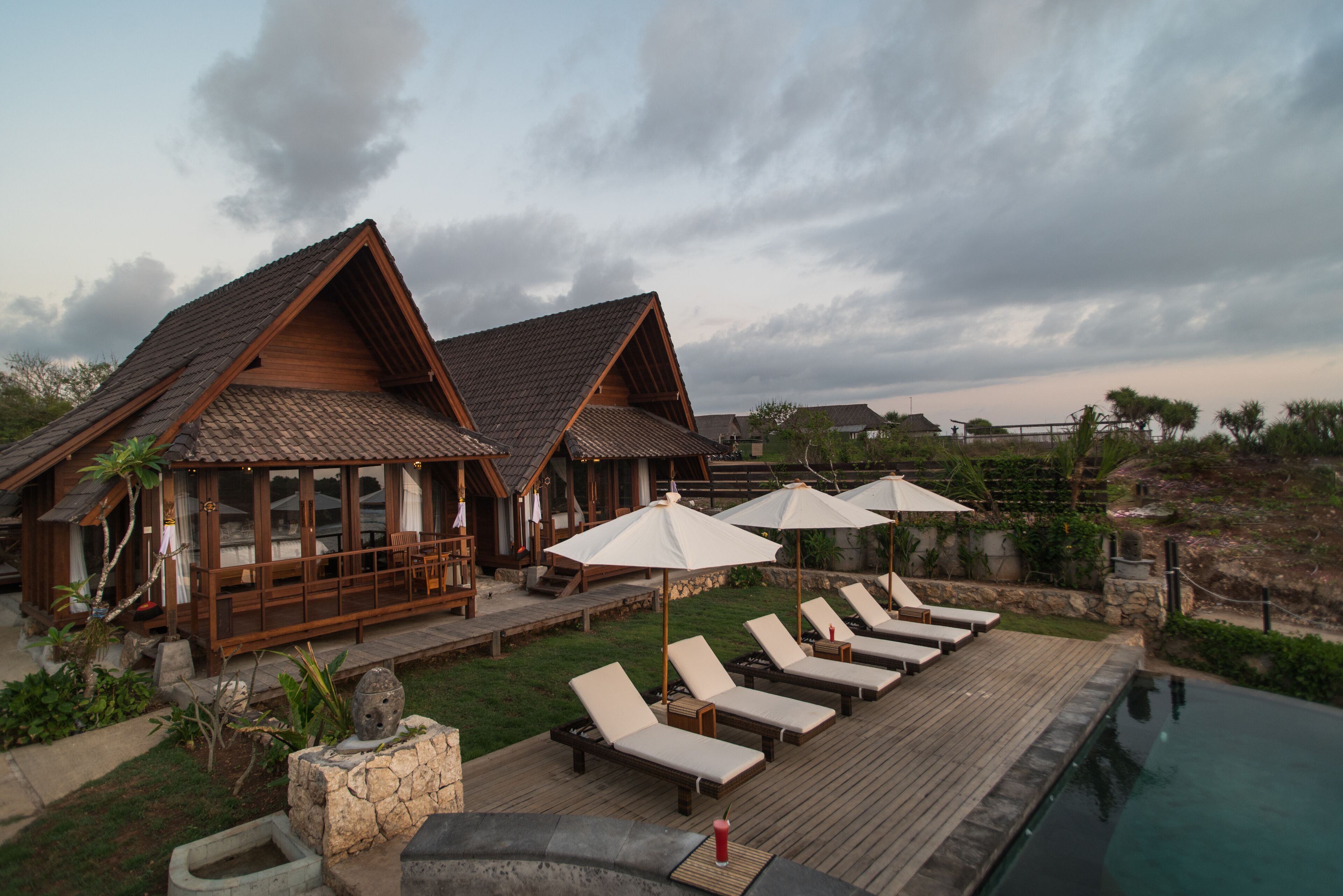 A wooden villa with a pool, lounge chairs, and umbrellas.