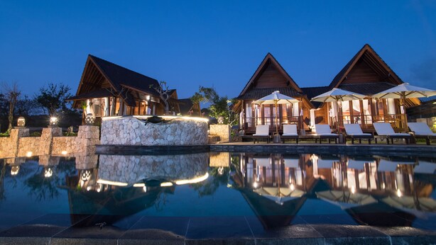 A resort with a swimming pool, wooden cabins, and lounge chairs.