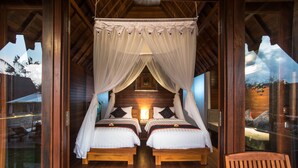 A bedroom with two beds, wooden flooring, and a canopy bed.
