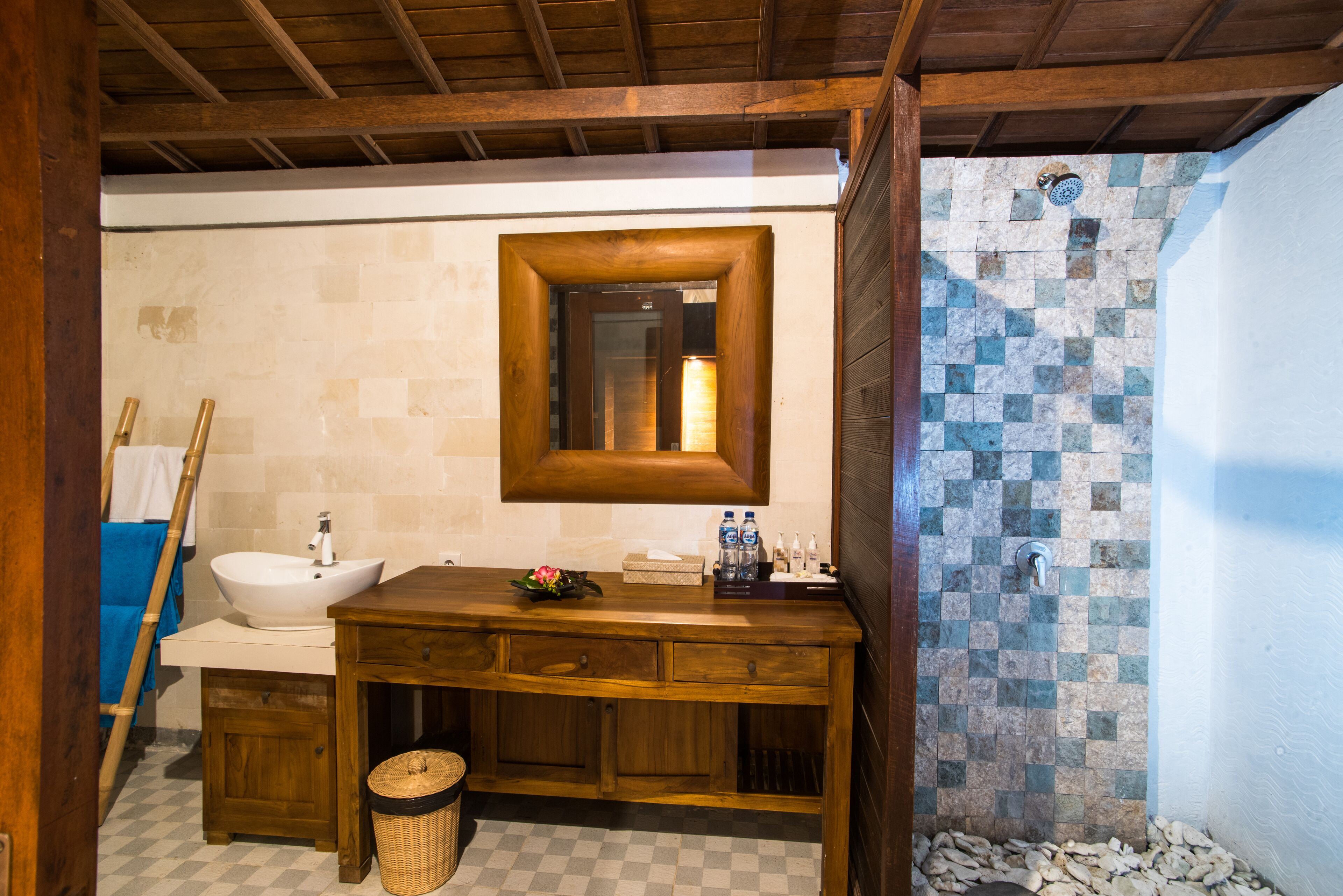 A bathroom with a wooden vanity, a white sink, a mirror, and a mosaic shower wall.