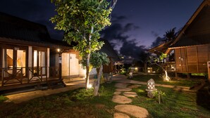 A well-lit courtyard with stone pathways, wooden buildings, and a tree.