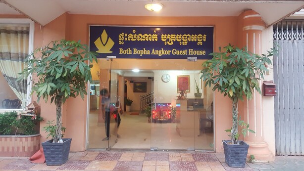 The entrance to Both Bopha Angkor Guest House with a clear glass door, potted plants on either side, and a signboard above the door. - Both Bopha Angkor (Siem Reap)