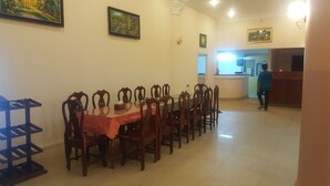A dining area with a rectangular table and wooden chairs, a black shelf unit, and a kitchen area in the background. - Both Bopha Angkor (Siem Reap)