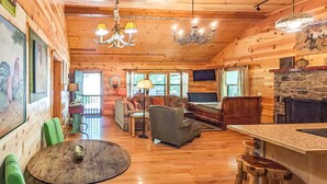 A cozy cabin interior with wooden walls, a stone fireplace, a dining area with a round table, and a living room with a sofa and chairs. - Blanchard Cabin in the Woods ~ close to caverns (Mountain View)