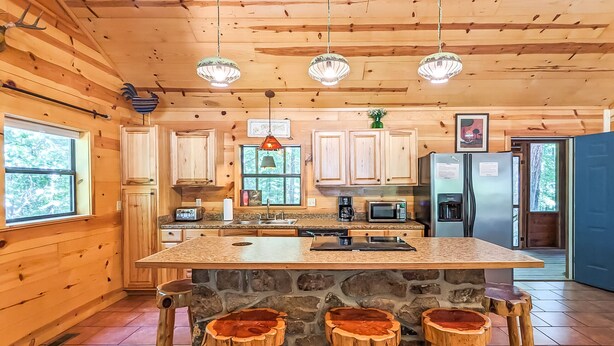 A wooden cabin kitchen with a large island, stone accents, and rustic stools. - Blanchard Cabin in the Woods ~ close to caverns (Mountain View)