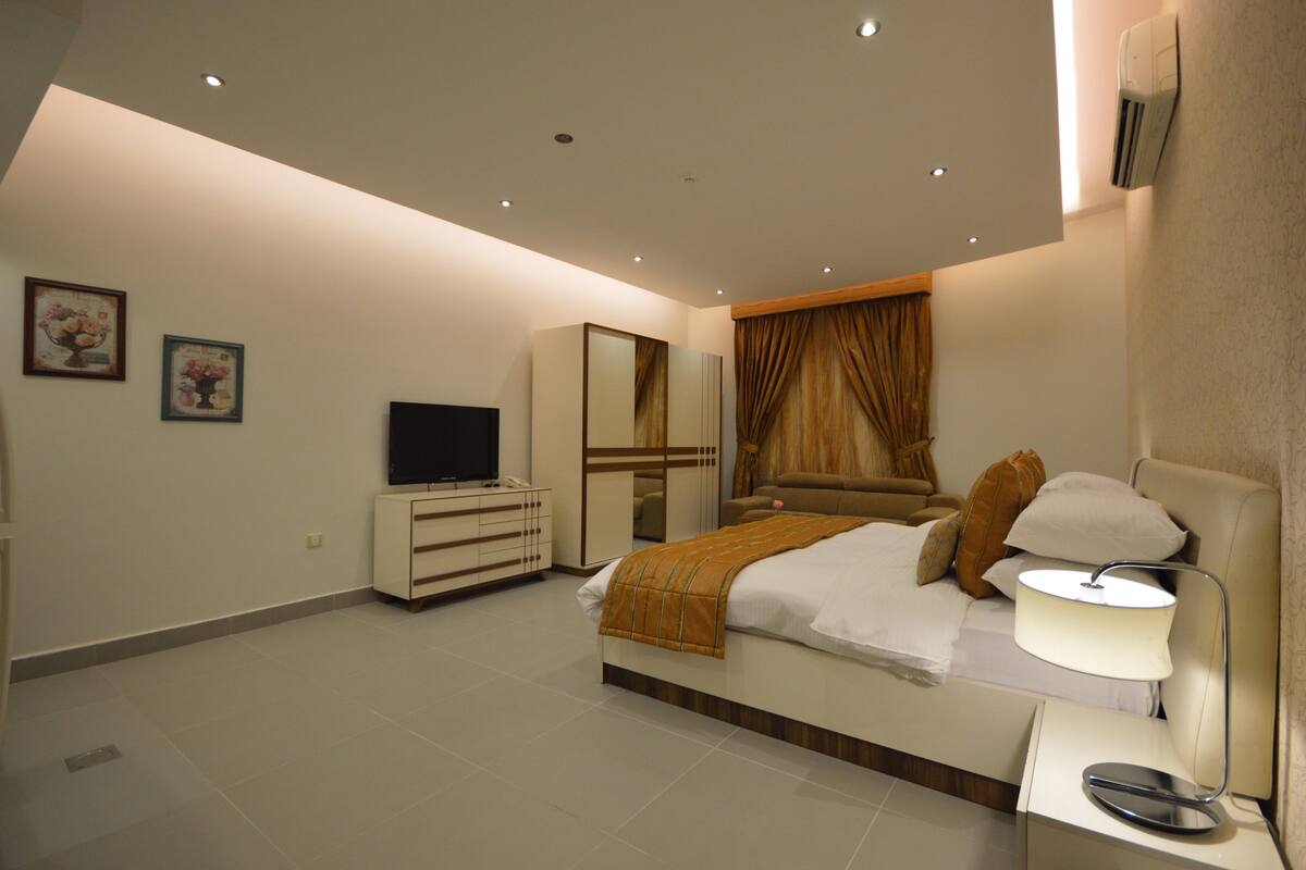 Ein modernes Schlafzimmer mit Bett, Nachttisch, Fernseher, Kleiderschrank und Spiegel.