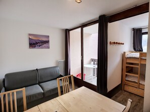 A room with a wooden table, a grey sofa, a small white table, a bunk bed, and a window with curtains. - Comfort Ski Soleil - 2P 4 ppl, Ski-in/Ski-out (Les Menuires)