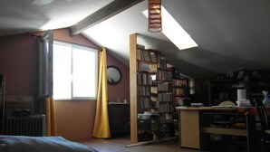 A room with a sloped ceiling, a bookshelf, a desk, a radiator, and a window with curtains. - Provencal farmhouse in a natural setting (Évenos)
