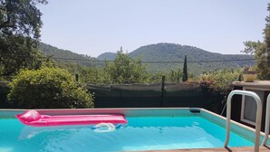 A swimming pool with a wooden deck in the foreground, surrounded by greenery and hills in the background. - Provencal farmhouse in a natural setting (Évenos)