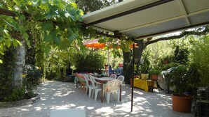An outdoor patio with a covered table and chairs, surrounded by potted plants and trees. - Provencal farmhouse in a natural setting (Évenos)