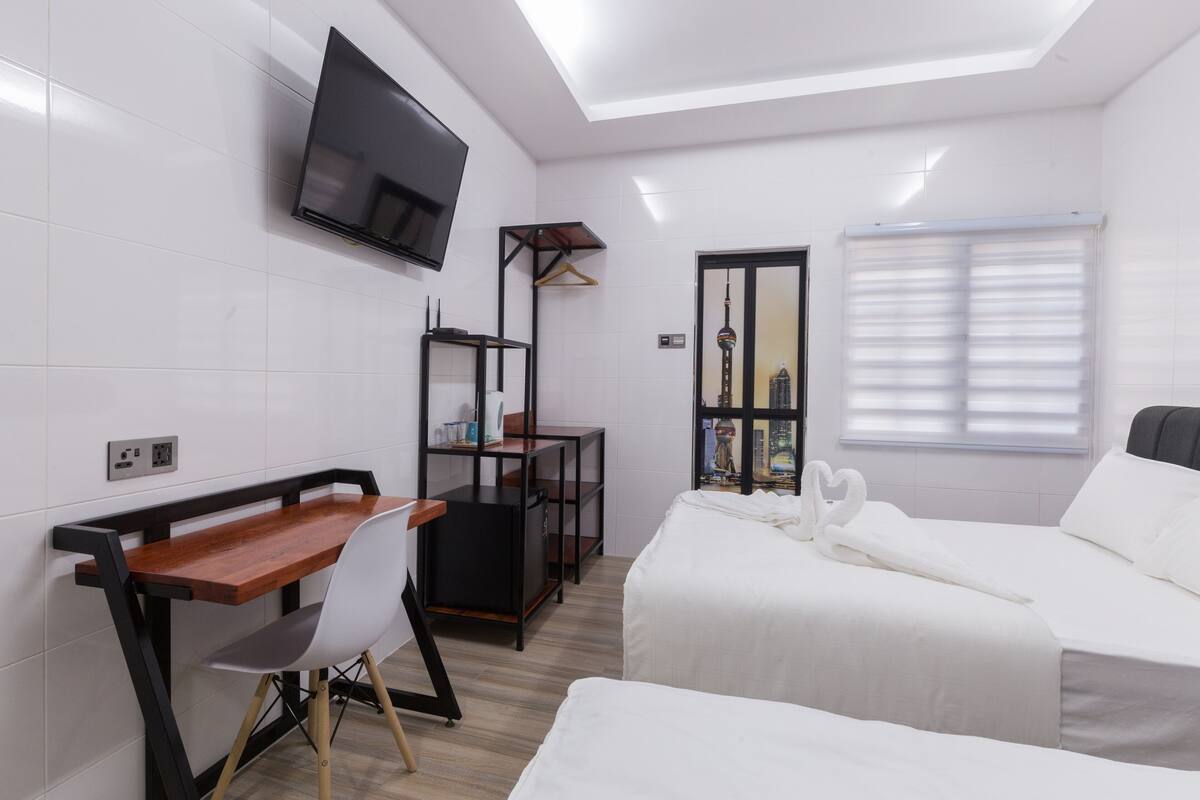 Camera d'albergo con un letto, una scrivania con sedia, una TV a parete e una finestra con persiane.