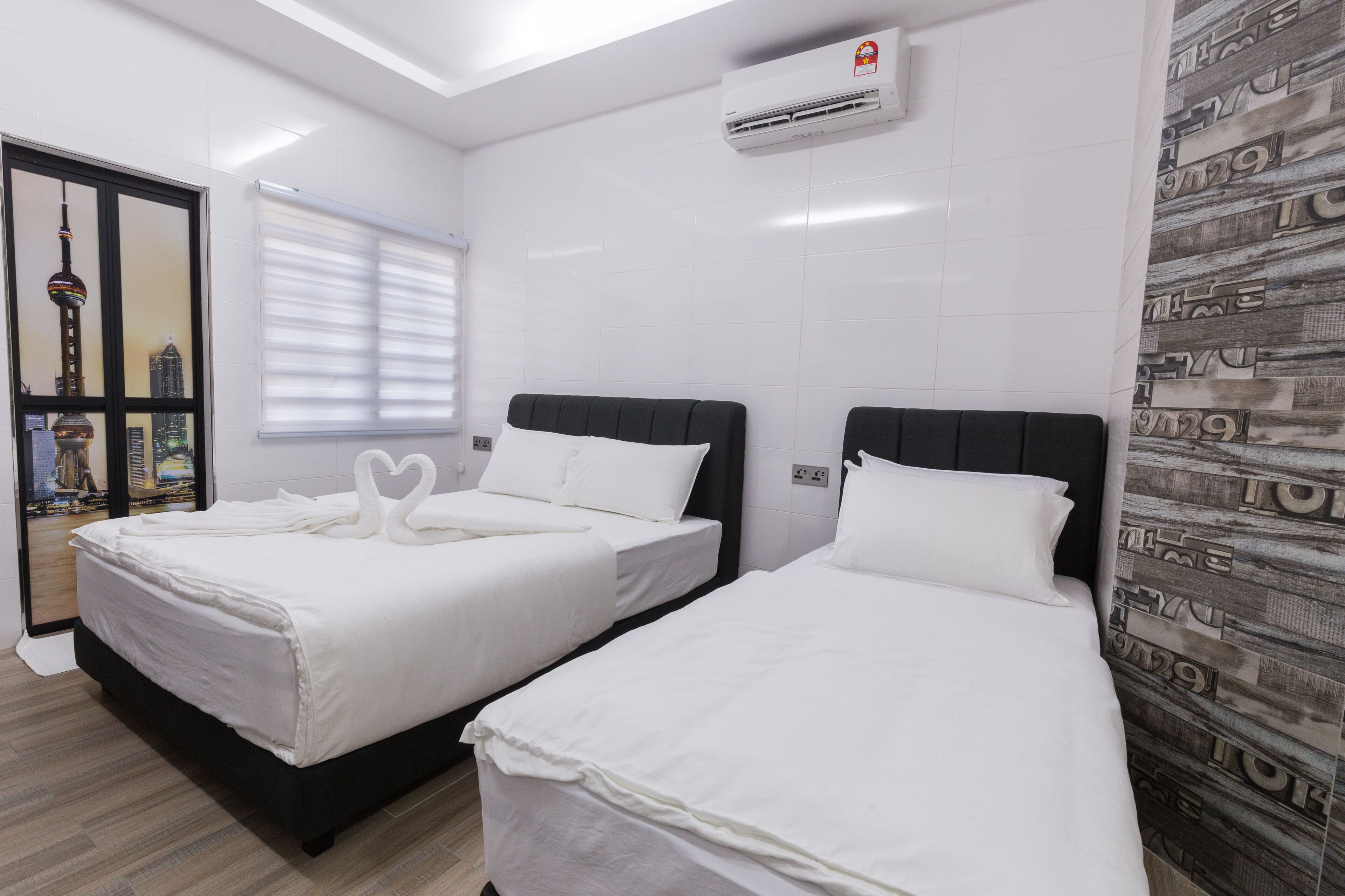 A hotel room with two beds, white bedding, a view of a cityscape through a window, and a wall-mounted air conditioner.