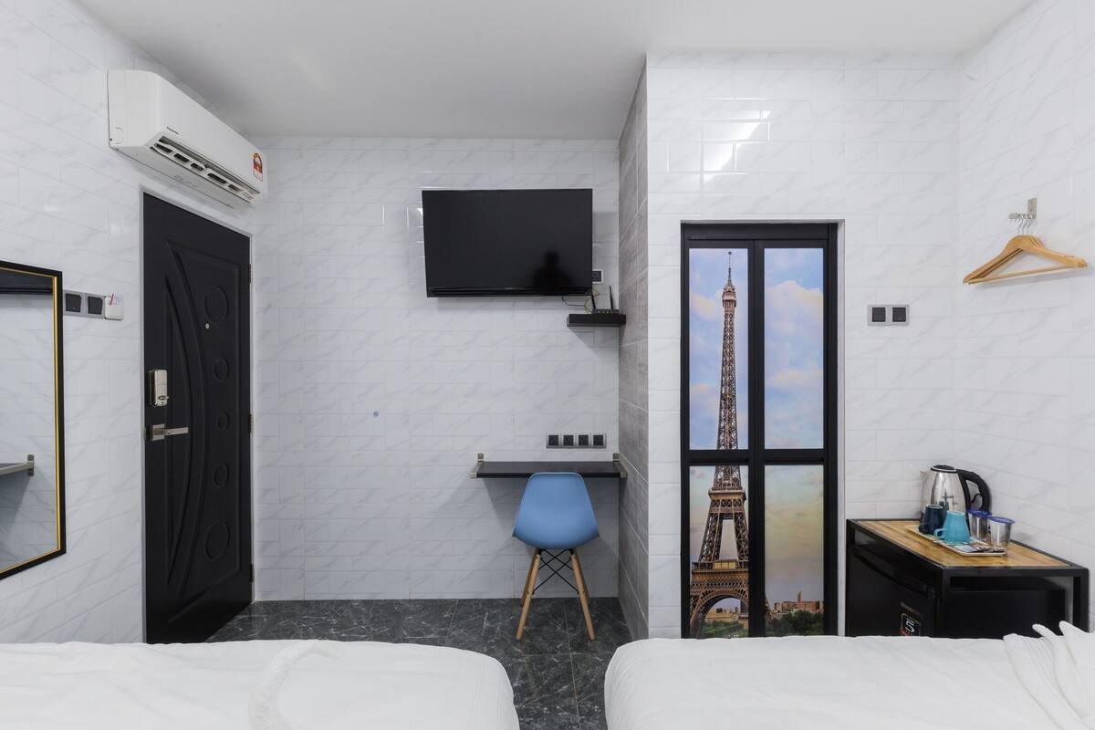 Una camera d'albergo con un letto, una scrivania, una sedia, una televisione, un armadio e vista sulla Torre Eiffel.