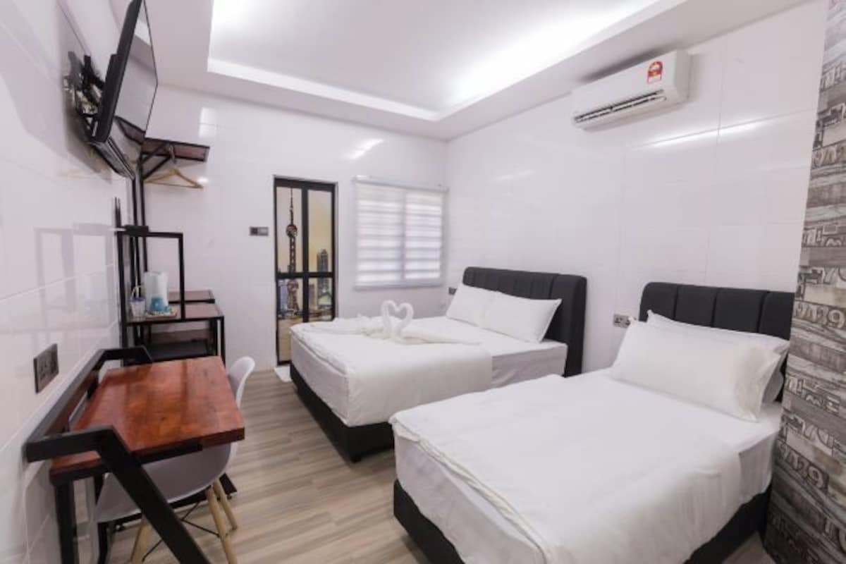 Une chambre d’hôtel avec deux lits, un bureau, une chaise et un téléviseur fixé au mur.