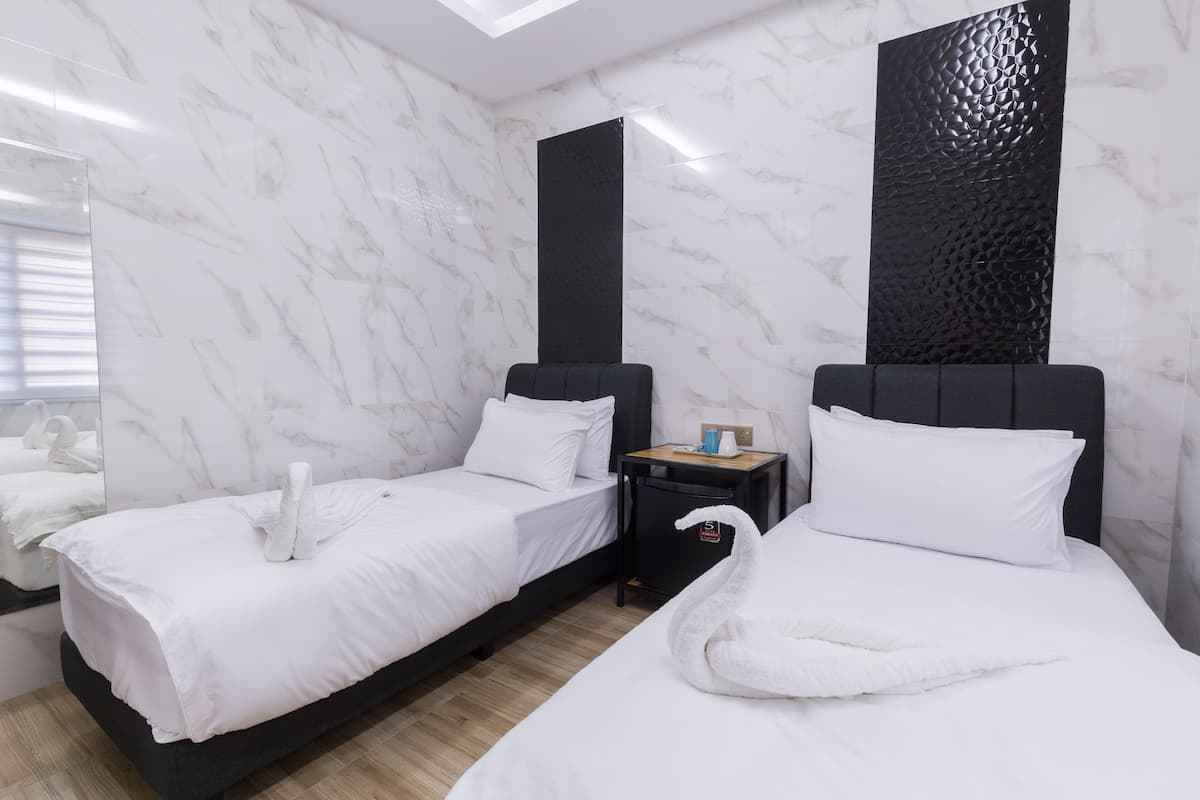 Camera d'albergo con due letti, pareti in marmo, un pannello nero strutturato, un comodino e uno specchio.