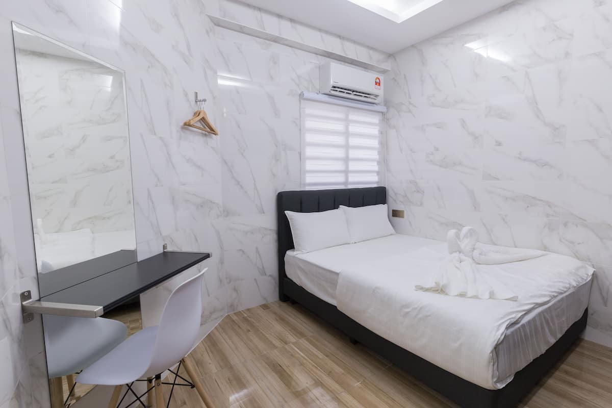 Camera d'albergo con parete in marmo, un letto con biancheria bianca, una scrivania con una sedia e un asciugamano appeso.