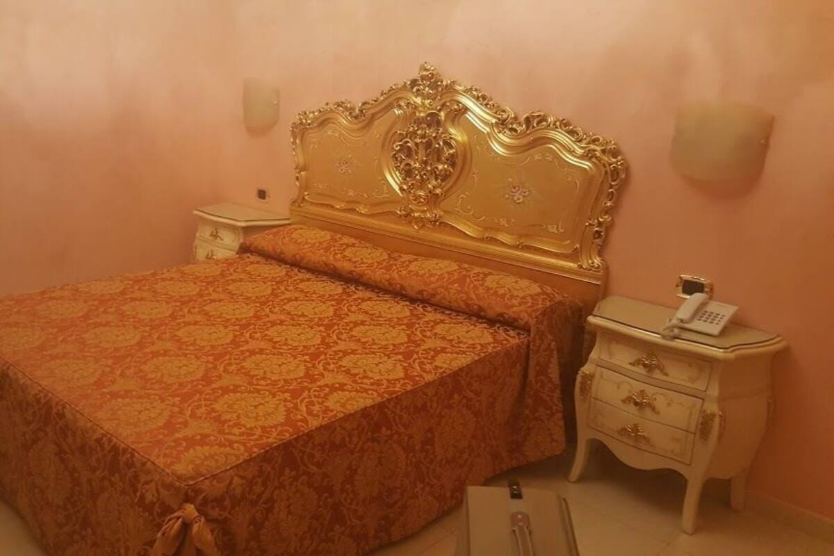 A bedroom with a large bed, ornate headboard, bedside tables, and a telephone.