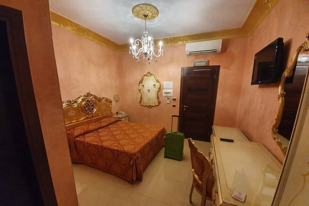 A bedroom with a bed, a desk, a chair, a television, and an air conditioning unit.