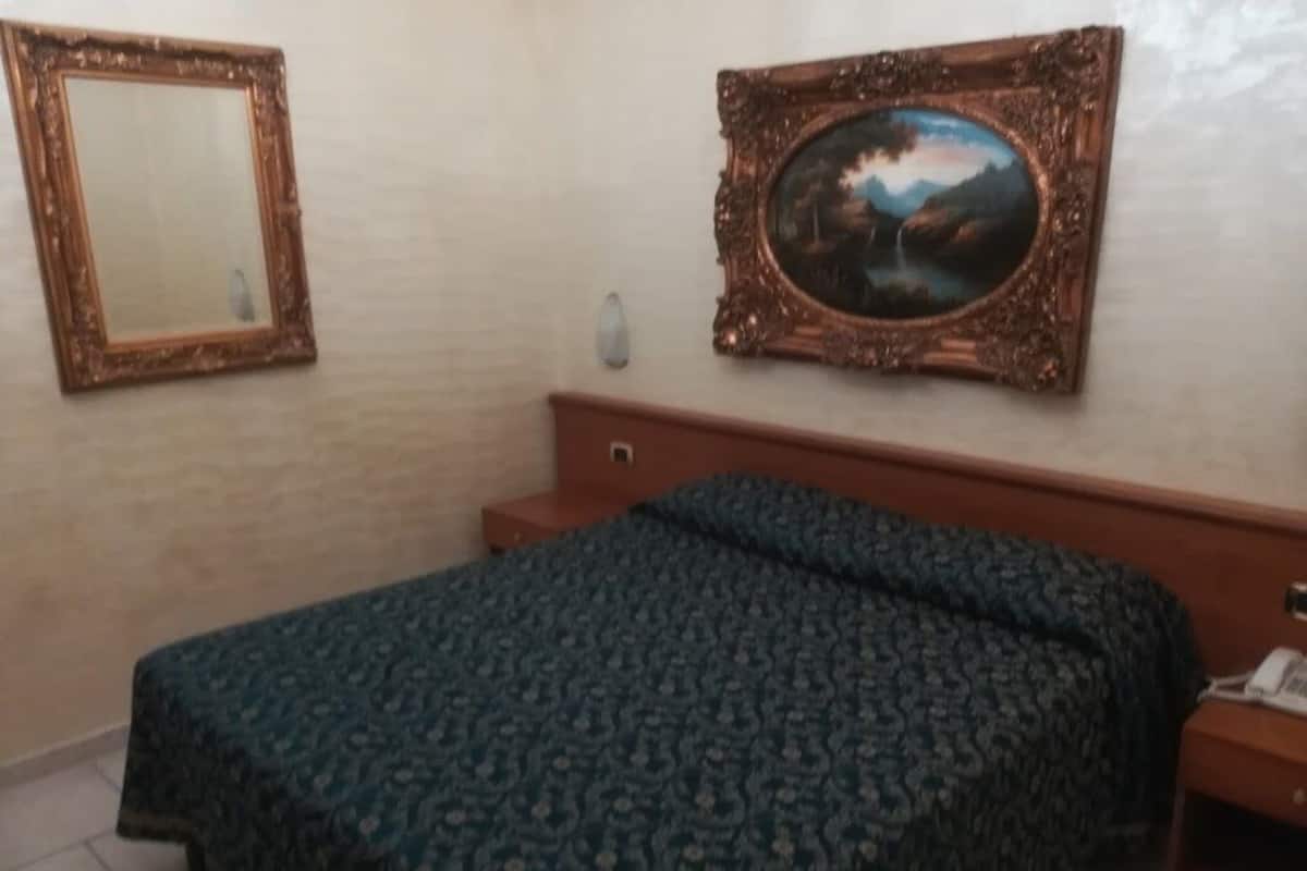 A room with a bed, a nightstand, a mirror, and a framed painting on the wall.
