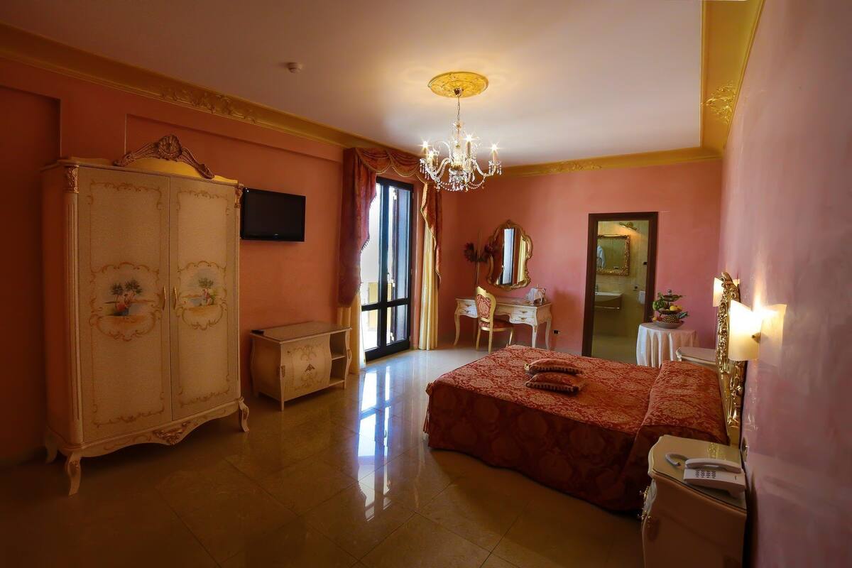 A bedroom with a large bed, a wardrobe, a desk, a chair, and a chandelier.