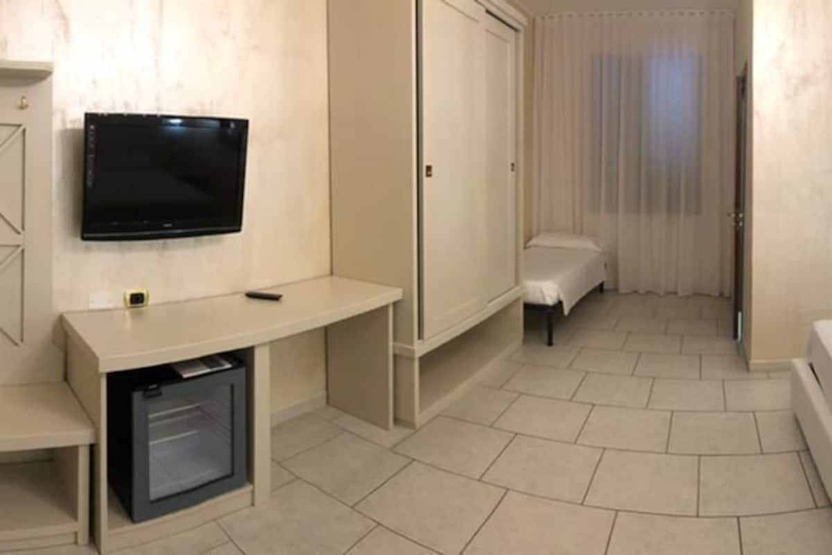 A hotel room with a bed, bedside tables, a TV, a desk, and a mirror.