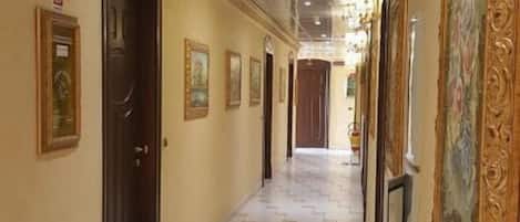 A hotel corridor with patterned flooring, framed artwork on the walls, and a ceiling with recessed lighting.