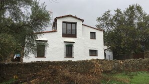 A white building with a tiled roof, a stone wall in front, and trees around. - Rural house El Lucero, in the heart of the mountains (full rental) (Alájar)