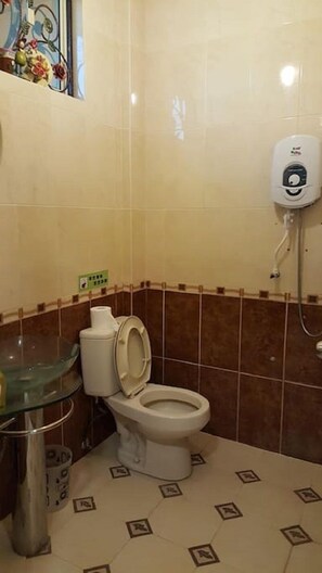 A small bathroom with a toilet, a glass sink, and a soap dispenser. - Seladah Stay (Kuching)