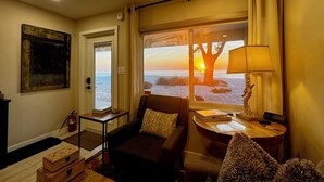Ett mysigt rum med utsikt över solnedgången över havet, en bekväm soffa, ett litet bord med en lampa och en brandsläckare på väggen.