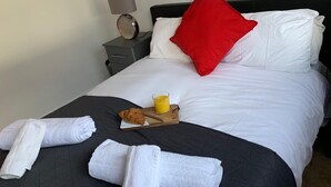 A neatly made bed with white and red pillows, a bedside table with a lamp, a tray with croissant and orange juice, and rolled white towels on the bed. - Apt. 4 at the Belvedere (Wolverhampton)