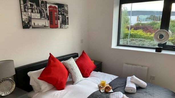 A neatly made bed with a black quilt, white and red pillows, and a breakfast tray with croissants and orange juice. - Apt. 4 at the Belvedere (Wolverhampton)