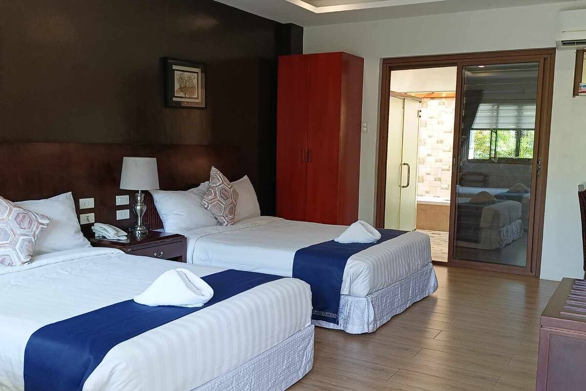 A hotel room with two beds, a wooden floor, a red wardrobe, and a door leading to a balcony.