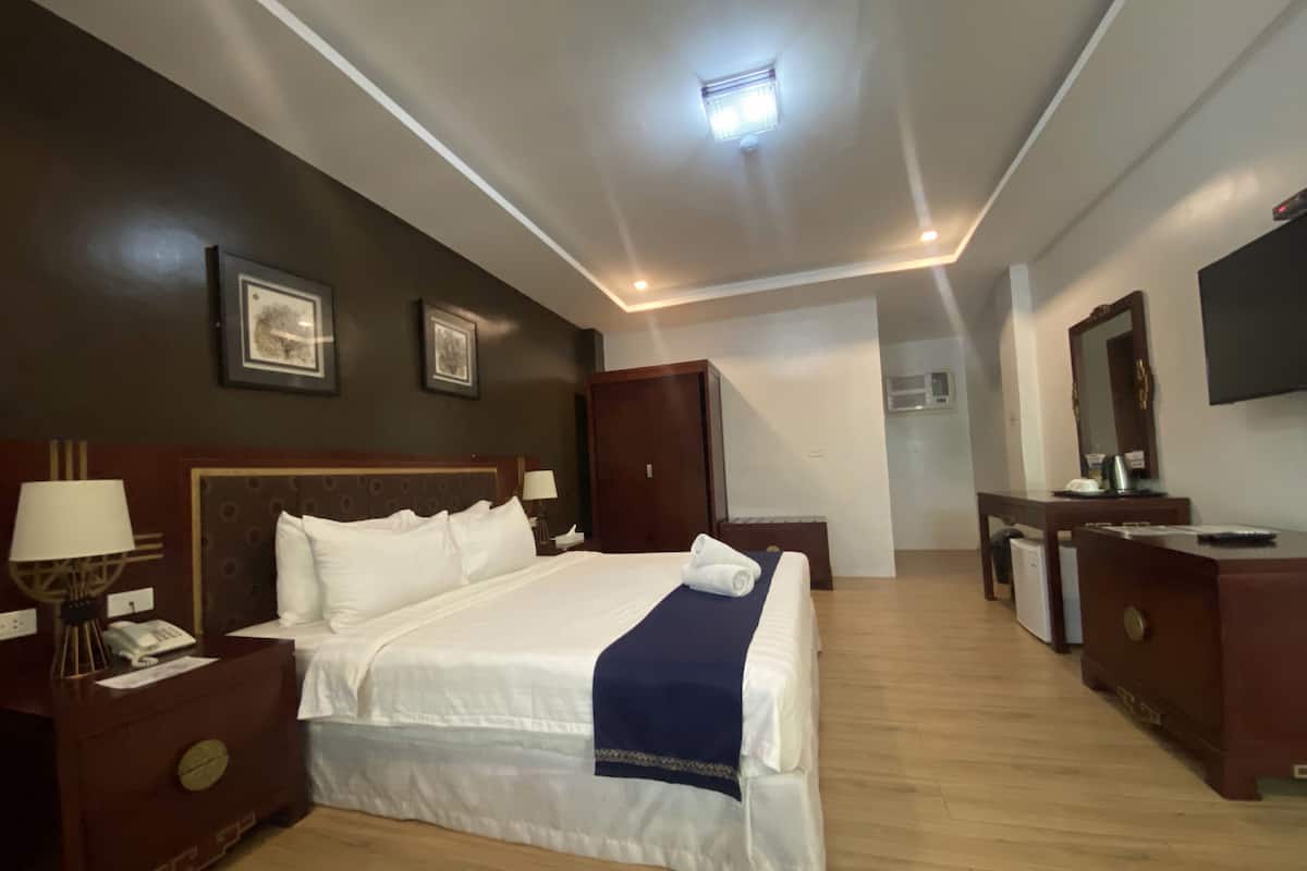 A hotel room with a large bed, bedside tables, a dresser, a mirror, and a television.