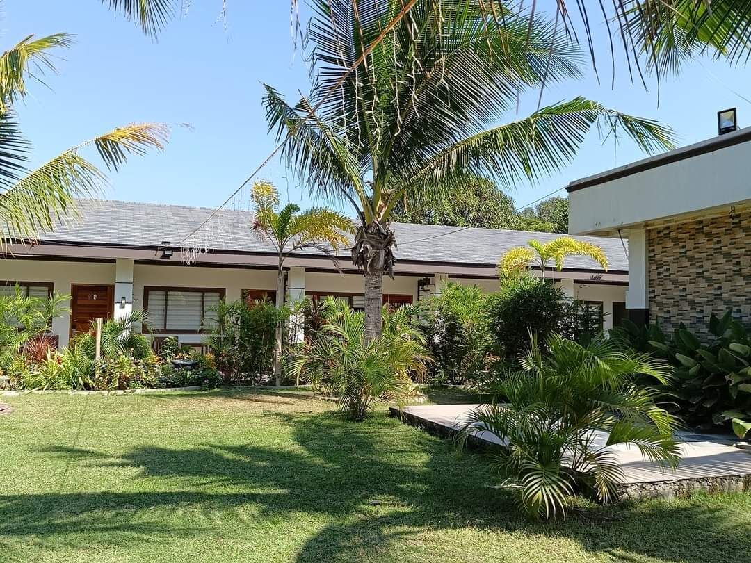 A two-story building with a flat roof, surrounded by a well-maintained lawn and various tropical plants.