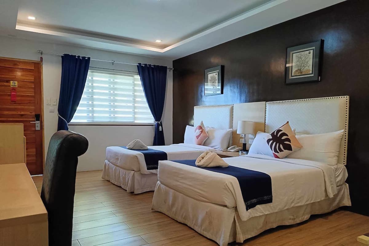 A hotel room with two beds, a desk, and a window with curtains.